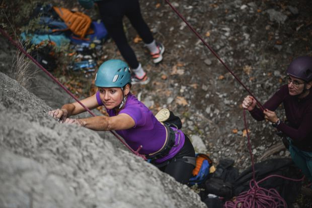 One rock climber hold the rope for another, illustrating a supportive research environment