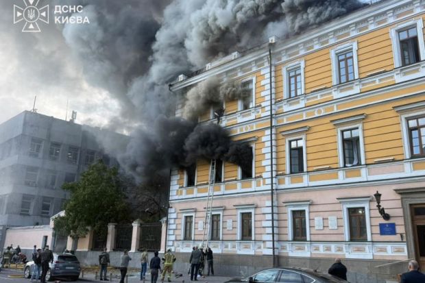 Heavy smoke billows out of a historic yellow and white building as a man tries to escape out of a window on the third floor