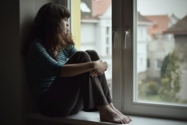 Sad young woman sitting on the window at home isolated, watching out. Coronavirus quarantine concept.