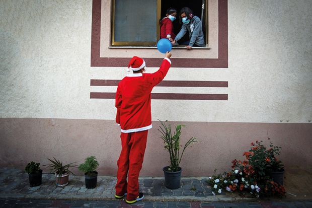 Man dressed as Santa passes a balloon to people through a window