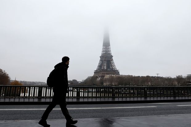 A man walks on a bridge across the Seine with the Eiffel Tower in the background A man walks on a bridge across the Seine with the Eiffel Tower in the background