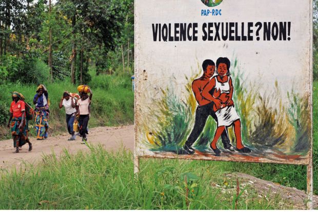 Congolese women walk past a sign opposing sexual violence