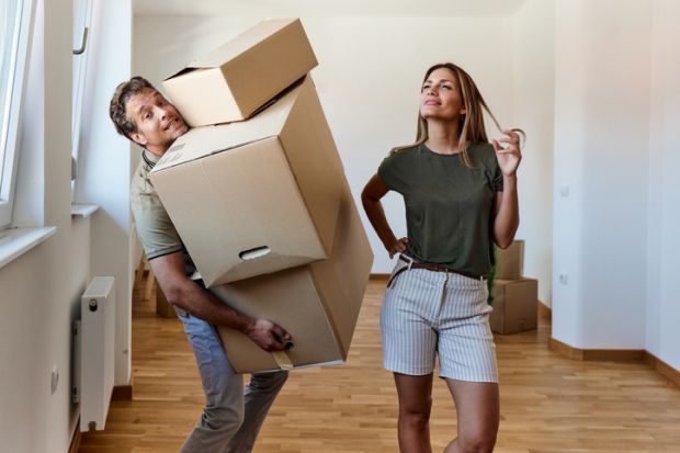 A man carries heavy boxes while a woman looks on A man carries heavy boxes while a woman looks on