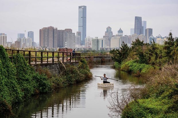 A man fishing on a polystyrene raft in Ma Tso Lung, Hong Kong, with the skyline of the Chinese mainland city of Shenzhen in the background.