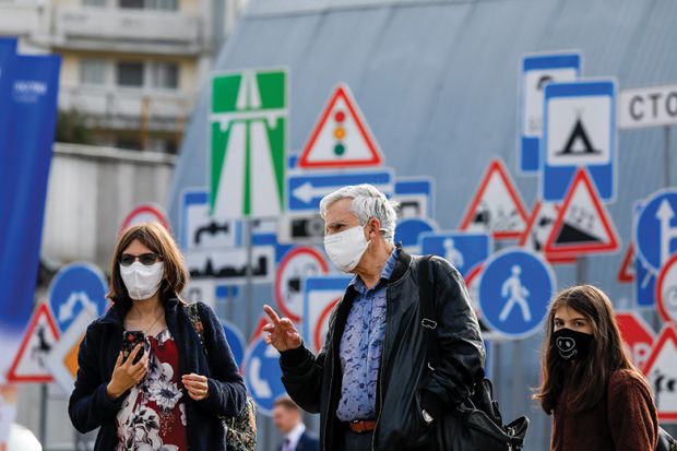 People in face masks in front of signs