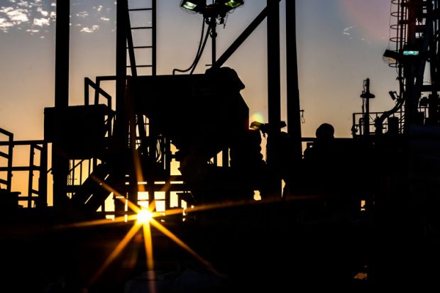 Silhouette of people working on oil rig at sunset