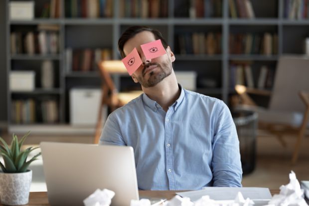 A business person sleeps with post-it notes of open eyes on his eyes