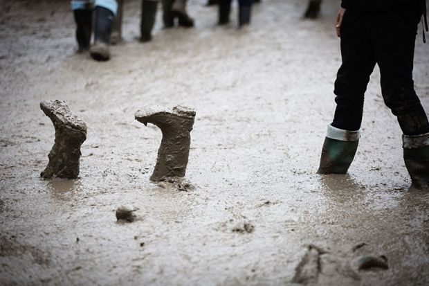 Festival goers in the rain and mud at the Glastonbury Festival, with boots upside down. To illustrate students could be left stranded if a major UK university went bust.