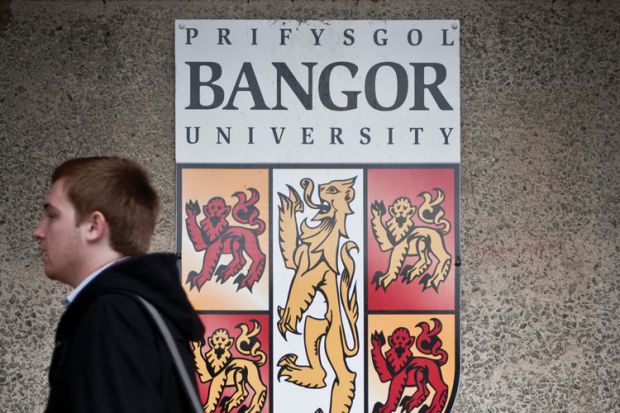 Student walking by Bangor University crest shield logo