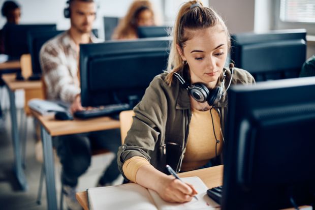 A university student writes notes while e-learning on a computer in the classroom A university student writes notes while e-learning on a computer in the classroom