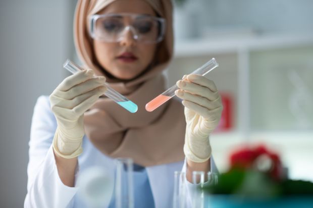 A woman holds up two test tubes containing differently coloured liquids