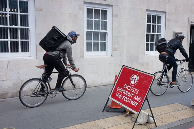Two delivery couriers ignore a cyclist's dismount sign