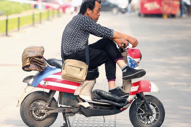 A Chinese man sits on a scooter decorated with America's Stars and Stripes outside a restaurant in Beijing on May 7, 2018. 