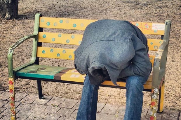 person hiding their head in their coat, sitting on a bench