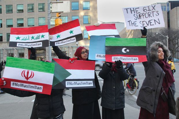 Muslim women hold signs with the flags of the banned countries during a massive protest against President Trump's travel ban outside of the U.S. Consulate in downtown Toronto