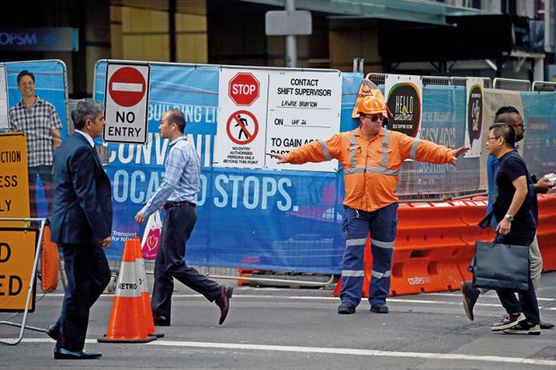 A worker directs pedestrians on a street in the central business district of Sydney