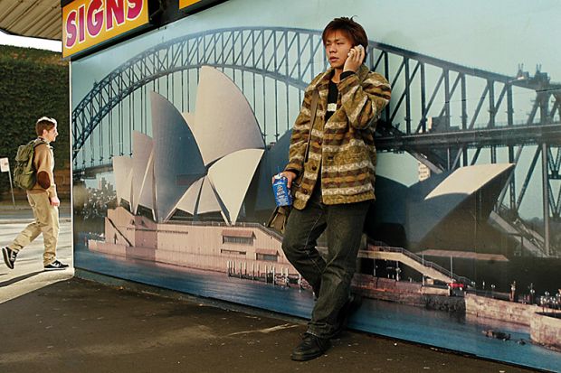 Asian student leaning against picture of Sydney Opera House, Australia
