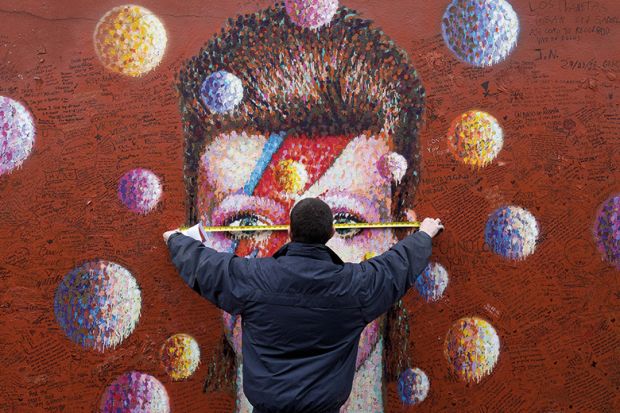 A workman measures up a mural of British musician David Bowie in Brixton, south London