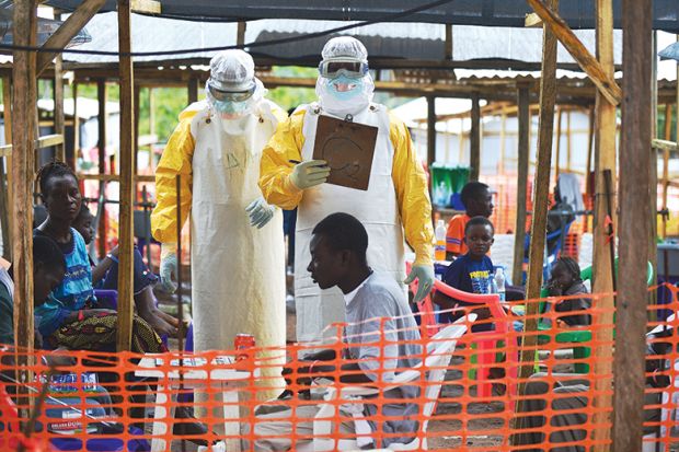 An MSF medical worker, wearing protective clothing relays patient details and updates behind a barrier to a colleague at an MSF facility in Kailahun, 2014. Kailahun along with Kenama district is at the epicentre of the world's worst Ebola outbreak