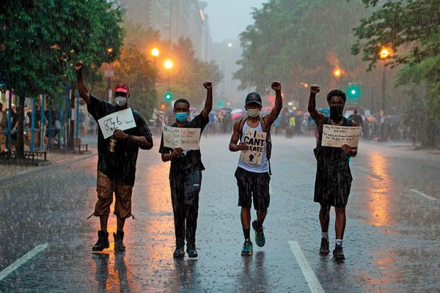 People holds signs as they walk in the rain after attending a Black Lives Matter protest in front of Lafayette Park next to the White House, Washington, DC on June 5, 2020