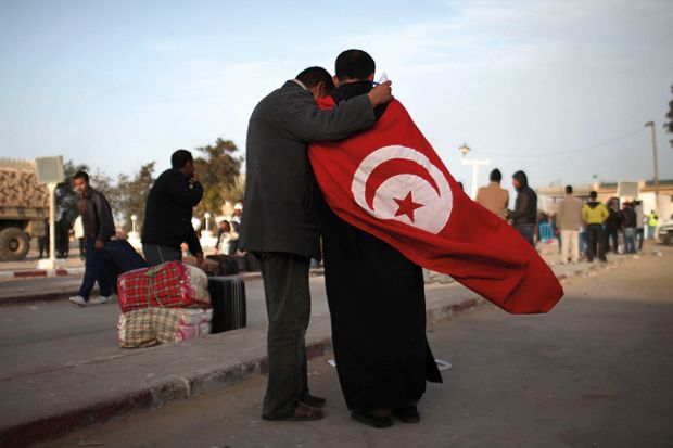 Two men, one wearing the flag of Tunisia, stand at the border of Libya on February 28, 2011 in Ras Jdir, Tunisia Two men, one wearing the flag of Tunisia, stand at the border of Libya on February 28, 2011 in Ras Jdir, Tunisia