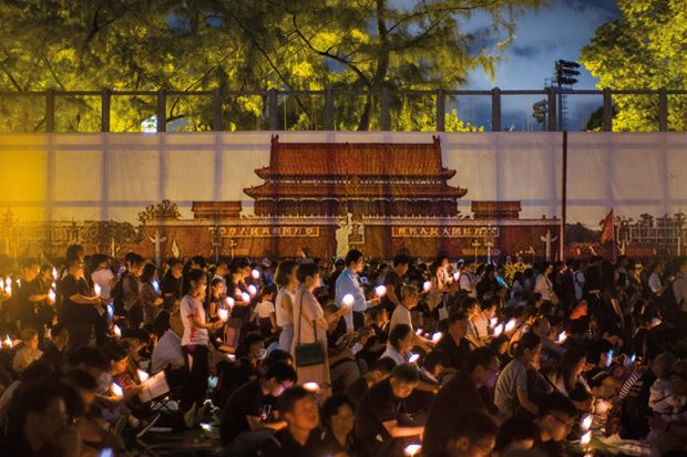 People hold candles in front of a backdrop showing  Beijing's Tiananmen Square during a vigil in Hong Kong on June 4, 2018