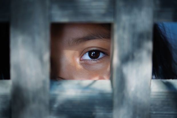The blank stare of the eye of a child who is standing behind what appears to be a wooden frame illustrating modern slavery