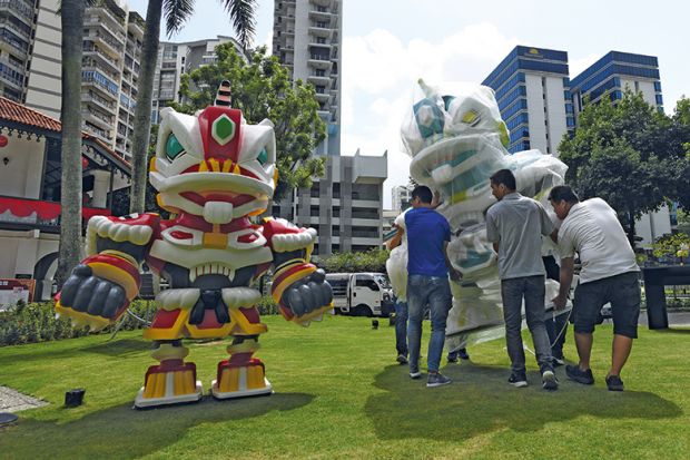 Workers carry a robot anime figure depicting the mask of a lion dance named "Lunar Guardians" in an outdoor installation at the Sun Yat Sen Nanyang Memorial Hall in Singapore