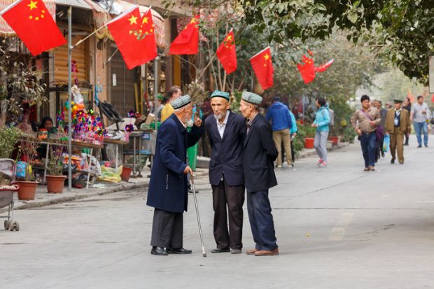 KASHGAR, XINJIANG / China - October 4, 2017: Three elderly men of the Uyghur minority having a conversation at a street in Kashgar Old Town. Chinese flags are mounted on the house in the background.