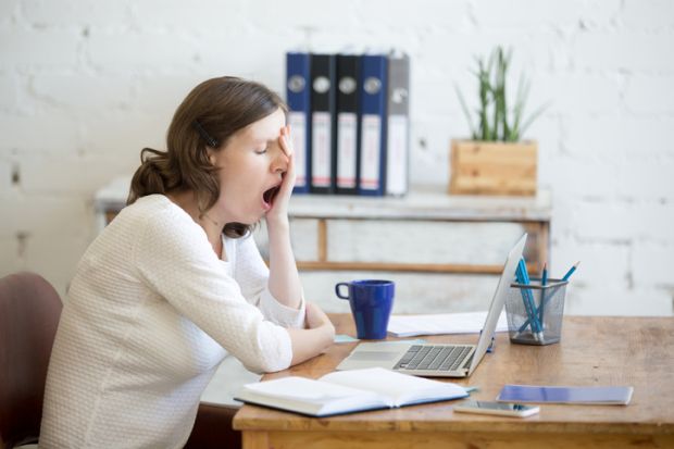 A woman yawns at a desk