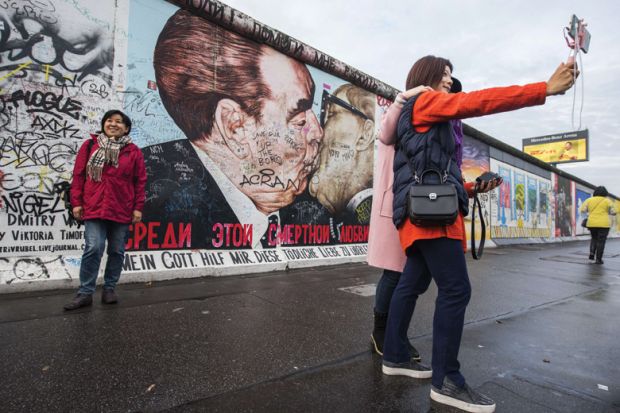 Tourists pose in front of Dmitri Vrubel mural, Berlin Wall