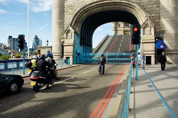 A cyclist, motorbikes and pedestrians wait as Tower Bridge in London is opened