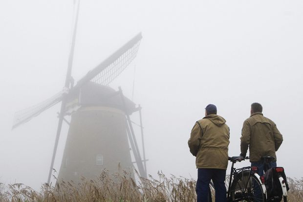 Two cyclists standing in fog looking at windmill