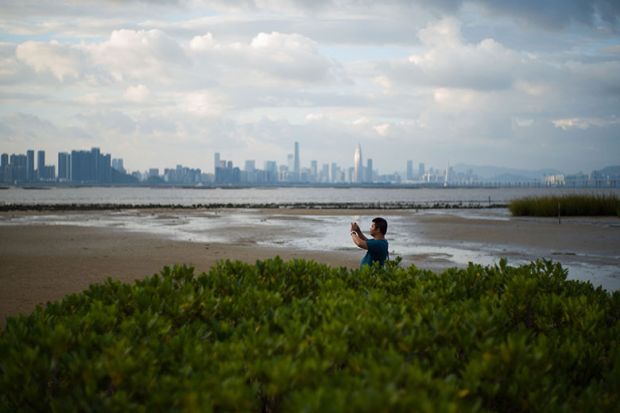 A man takes a photo from the shoreline of Hong Kong’s Deep Bay with the skyline of Chinese mainland city of Shenzhen visible behind him A man takes a photo from the shoreline of Hong Kong’s Deep Bay with the skyline of Chinese mainland city of Shenzhen visible behind him