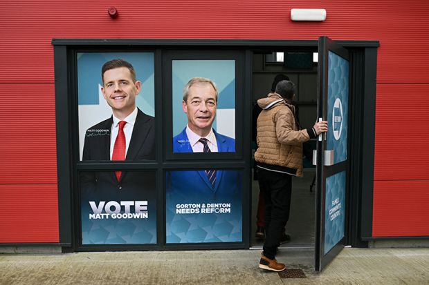 A person walks through a doorway printed with the faces of Reform UK candidate Matt Goodwin and Reform UK leader Nigel Farage during an event ahead of the February 26 Gorton and Denton by-election, in Denton, northwest England on 5 February, 2026. 
