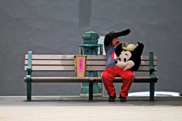 A street performer in a Mickey Mouse costume rests on a bench to illustrate We can’t stop the ‘rip-off degrees’ debate – but we can change its terms