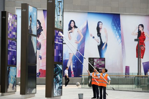 Two workers clean billboards outside a shopping mall in Beijing 