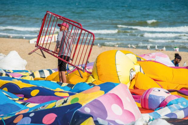 Man at work holding a gate walking on deflated balloons on Bournemouth beach in Dorset, England, UK.to illustrate Commit now to restoring ‘£7,000’ pension losses, say USS members