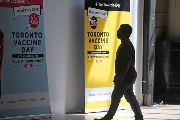 Person walks by Toronto Vaccine Day poster Person walks by Toronto Vaccine Day poster as metaphor for Canadian universities finally move to mandate vaccines