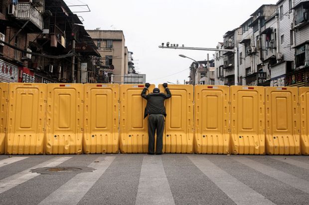 A man wearing a face mask talks to another man through a makeshift barricade wall in Wuhan, Hubei, China as a metaphor for China and Japan to keep borders shut for another term