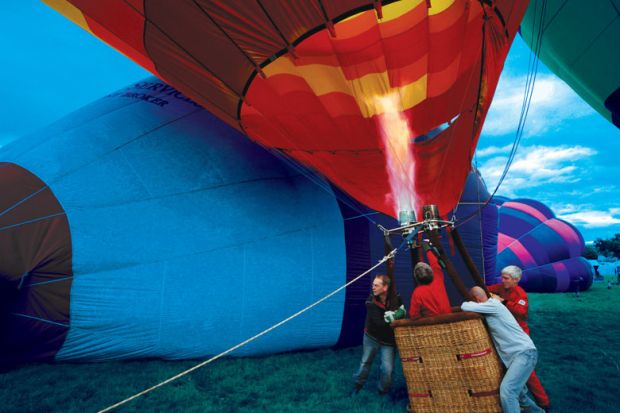 Balloonists hold down a basket as hot-air balloons begin to rise to illustrate Rising inflation will ramp up stratification in higher education
