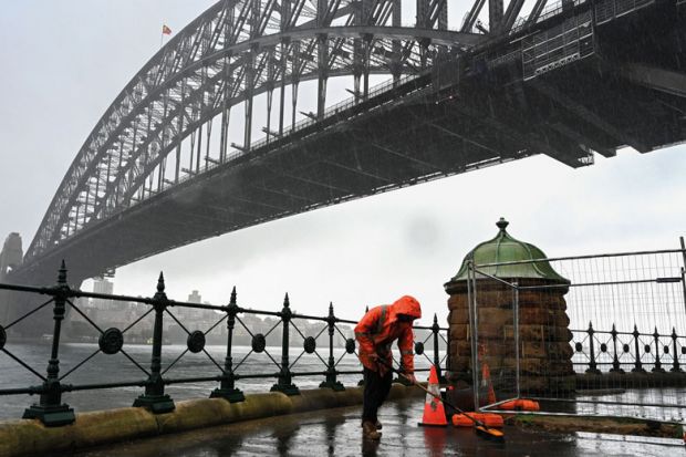 A construction worker sweeps away water while it rains next to the Harbour Bridge in Sydney to illustrate Shortened work rights ‘complicate’ skills drive