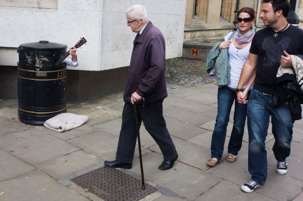 A street busker hides in a litter bin to illustrate Professor to sue Cambridge over ‘forced retirement’ rules