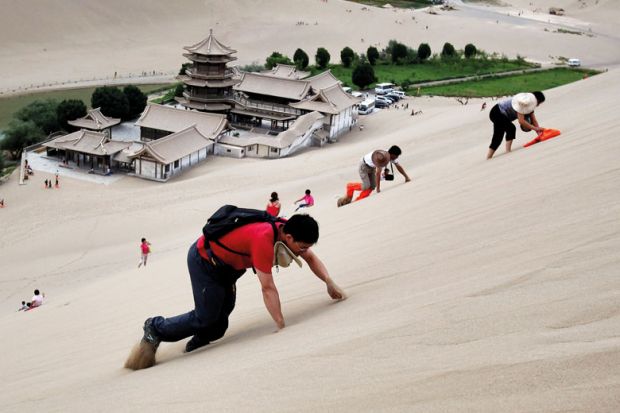 Tourists climb the Singing Sand Dunes near the Crescent Moon Spring