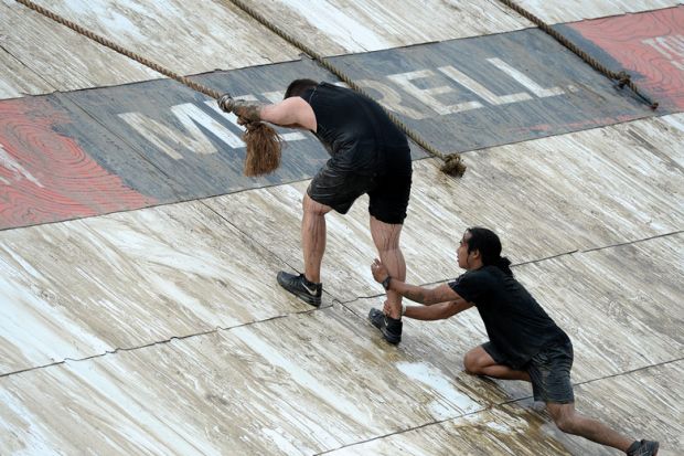 Climbing the final obstacle during a Tough Mudder race to illustrate US academia ‘will never reach racial parity’ on current progress