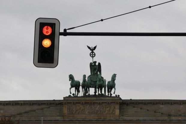 A traffic light with red and yellow signs is pictured in front of the Brandenburg Gate to illustrate New German government promises university funding boost