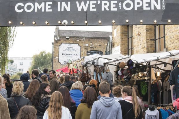 crowds passing under an entrance sign reading " Come in We're (very) Open.