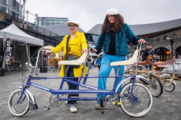 Two ladies in vintage clothing pose with a tandem Raleigh Chopper in Granary Square, Kings Cross to illustrate ‘Shut gender pay gap with v-c job-shares’