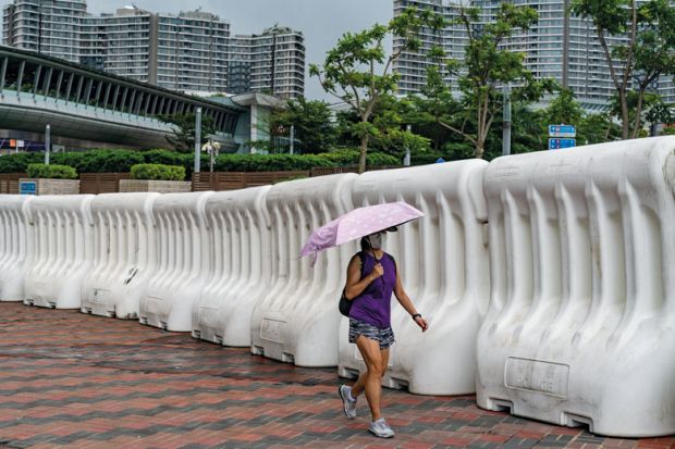 A woman holding an umbrella walks in front of water barrier soutside the West Kowloon