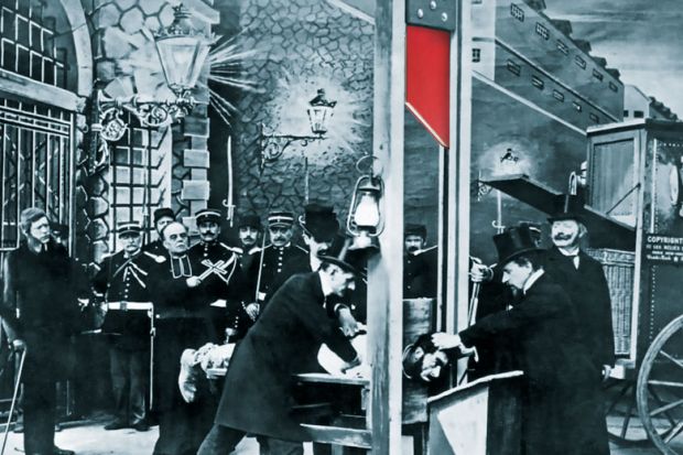 French postcard about 1900 showing a mock-up execution in a photographer's studio to illustrate Why should academics risk their livelihoods in contributing to books?